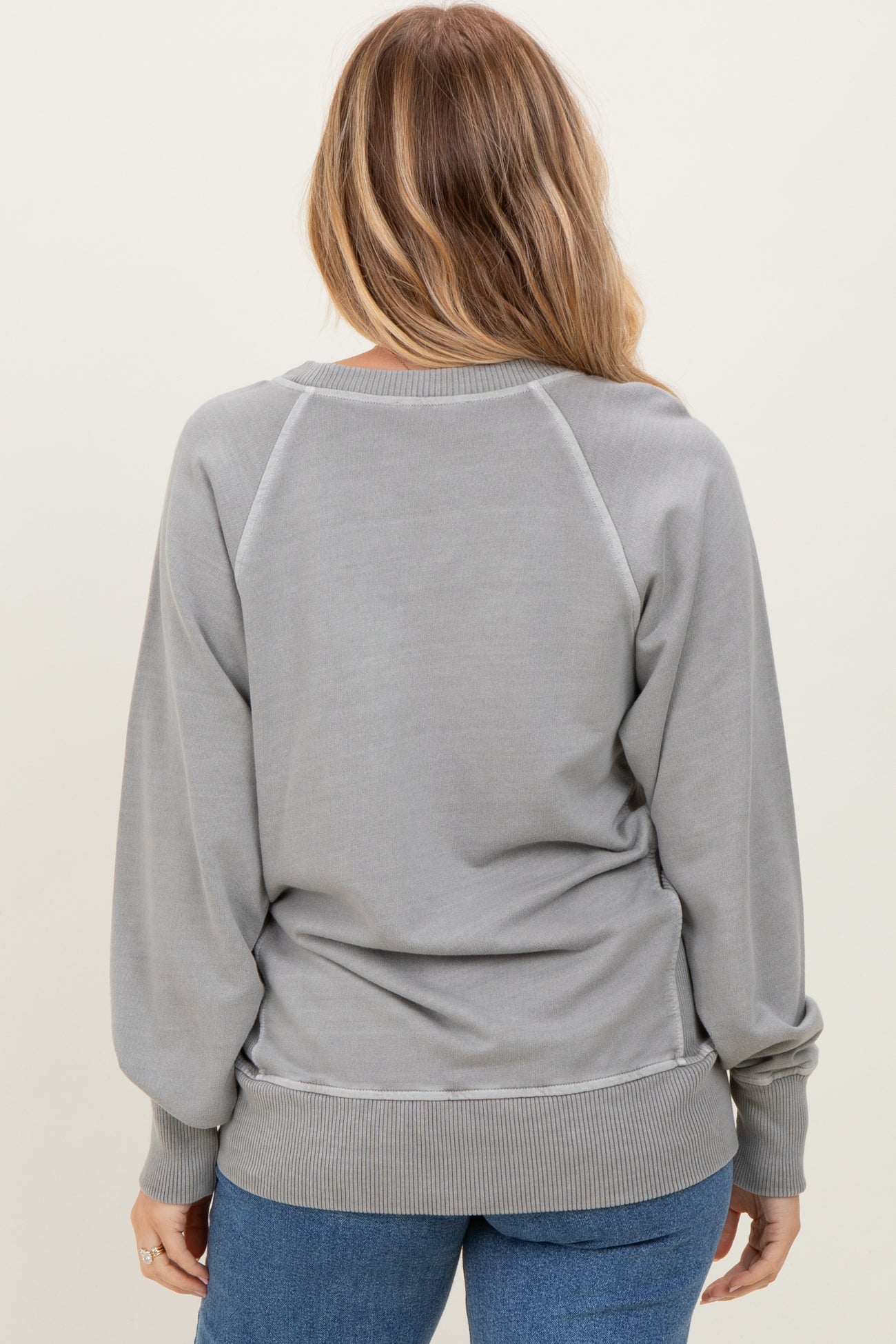 woman wearing a gray oversized sweatshirt with raglan sleeves and a relaxed fit, styled with blue jeans