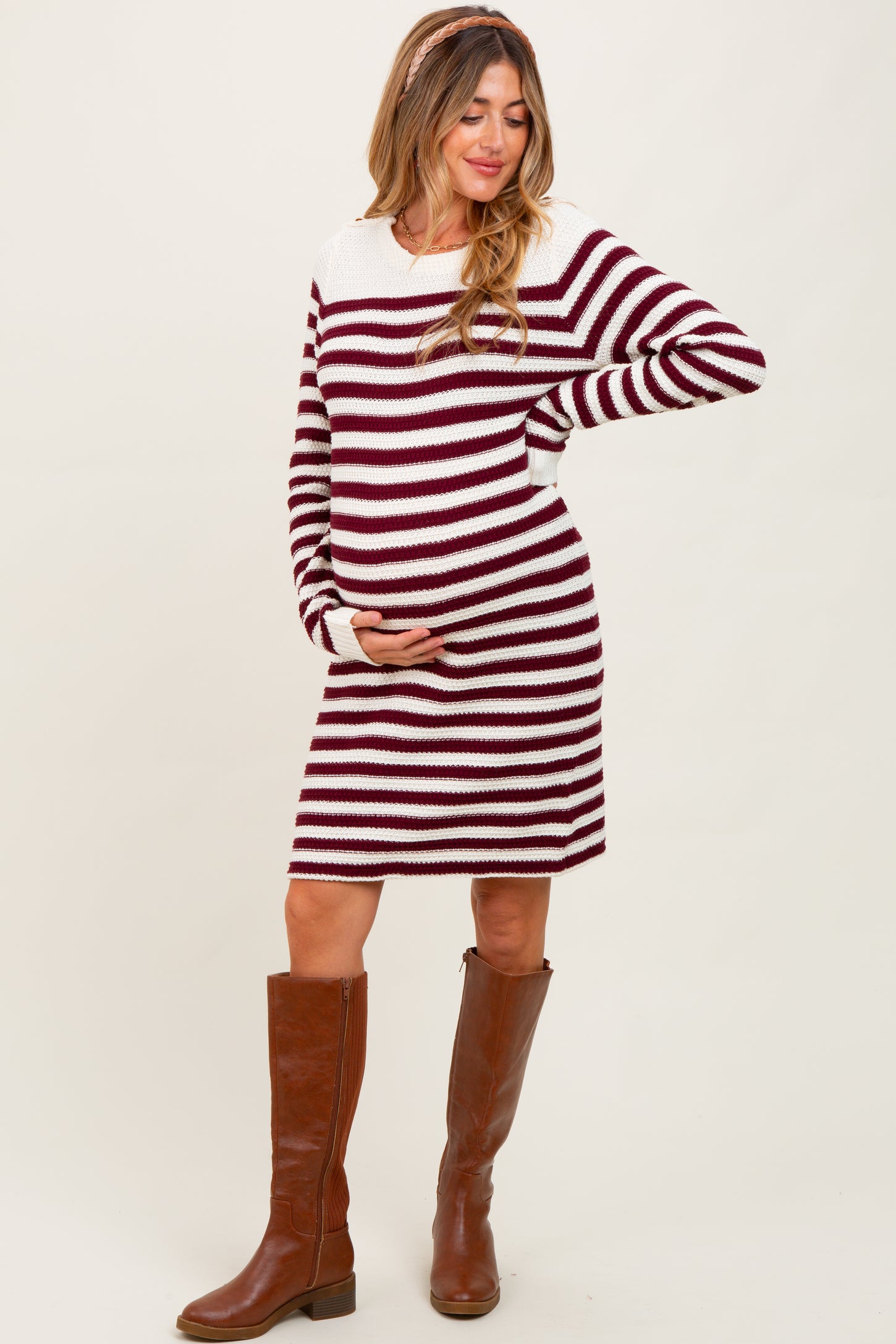 woman wearing a maroon and cream striped maternity sweater dress and holding her baby bump