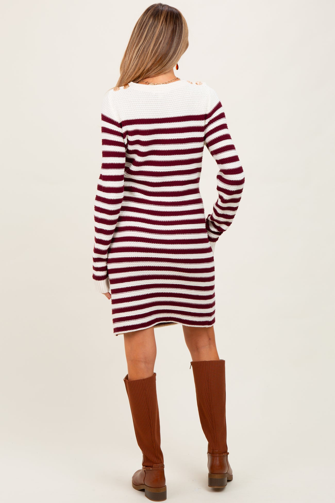 woman wearing a maroon and white striped maternity sweater dress, standing with her back to the camera