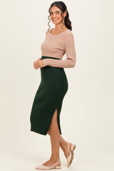 woman wearing a ribbed beige long sleeve top and a dark green midi skirt with a side slit