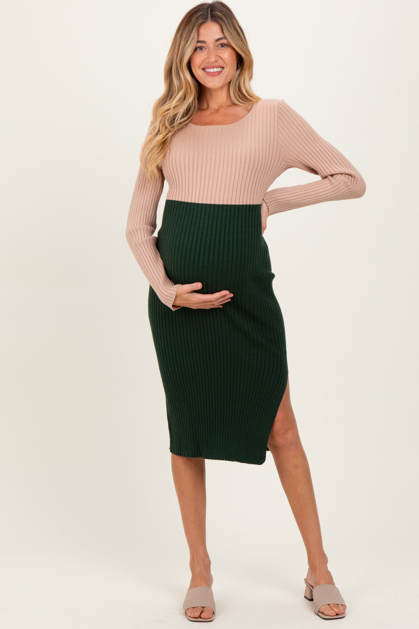 woman wearing a color-blocked maternity dress with a light pink top and dark green skirt, showing her baby bump
