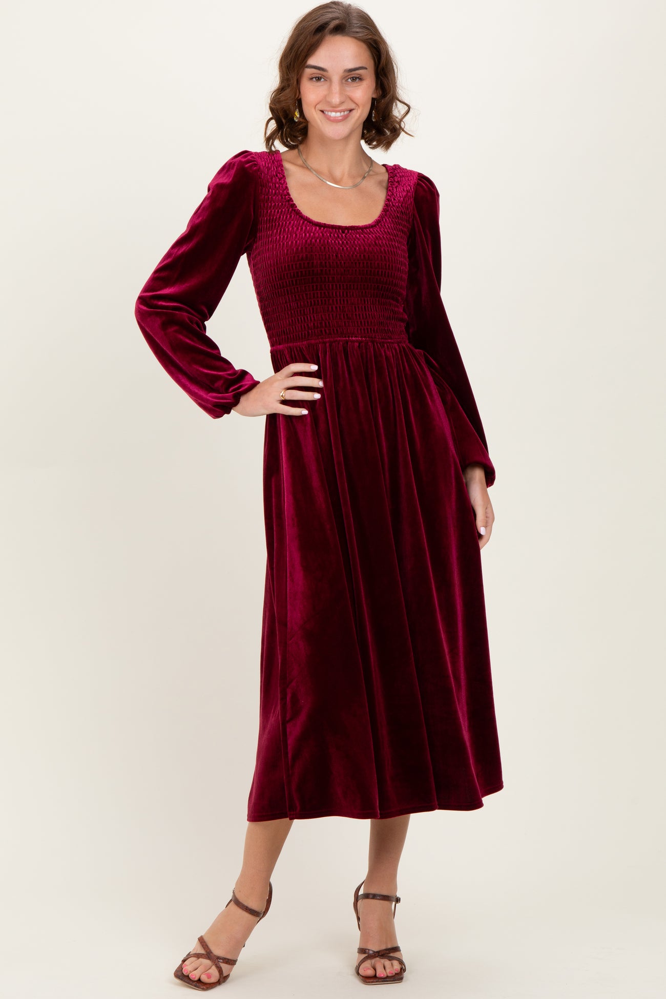 woman wearing a burgundy long sleeve velvet dress with a smocked bodice and a flowing skirt