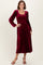 woman wearing a burgundy long sleeve velvet dress with a smocked bodice and a flowing skirt
