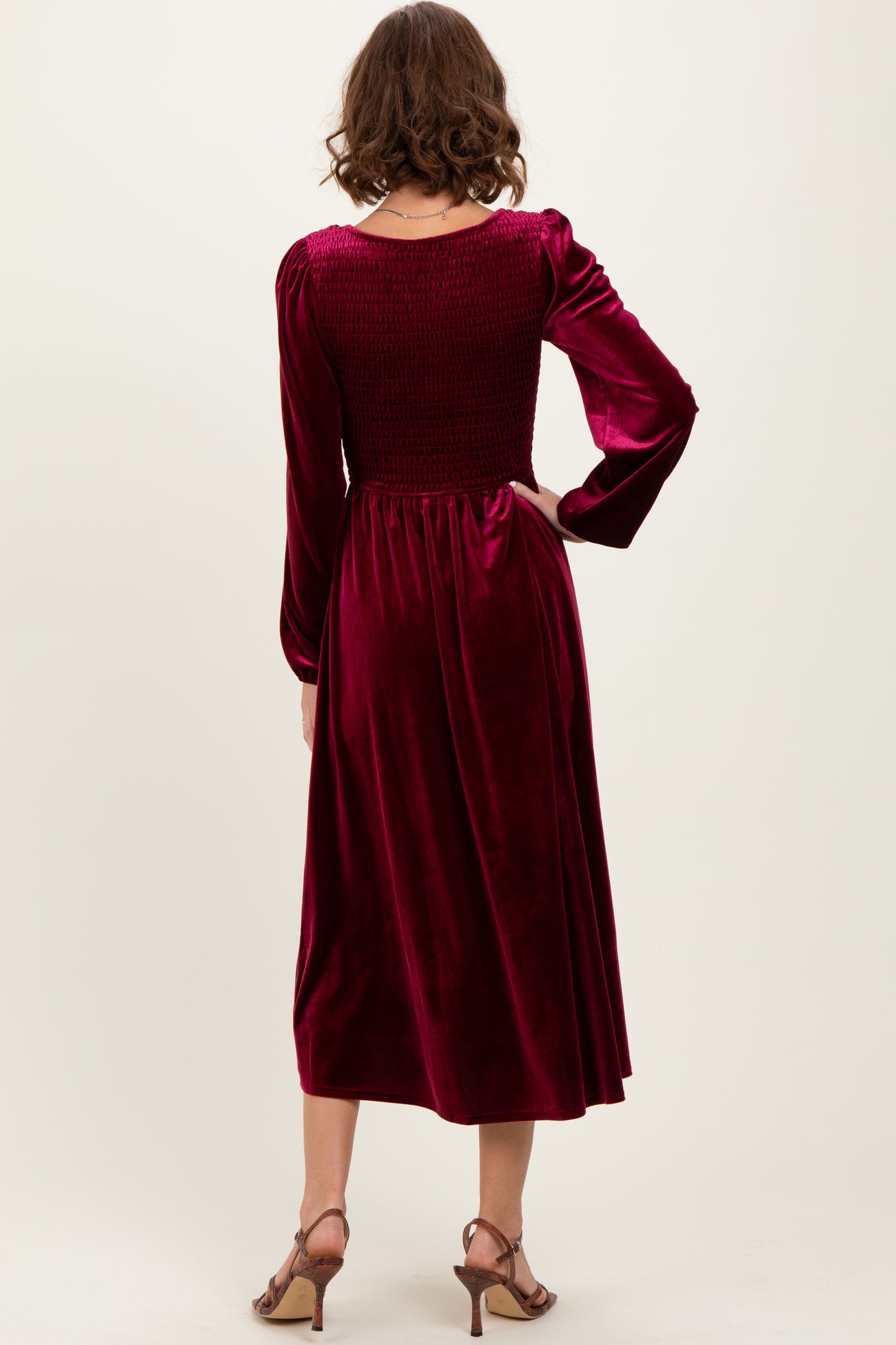 woman wearing a burgundy velvet dress with a smocked bodice and long sleeves, standing with her back to the camera