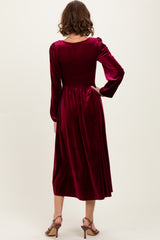 woman wearing a burgundy velvet dress with a smocked bodice and long sleeves, standing with her back to the camera