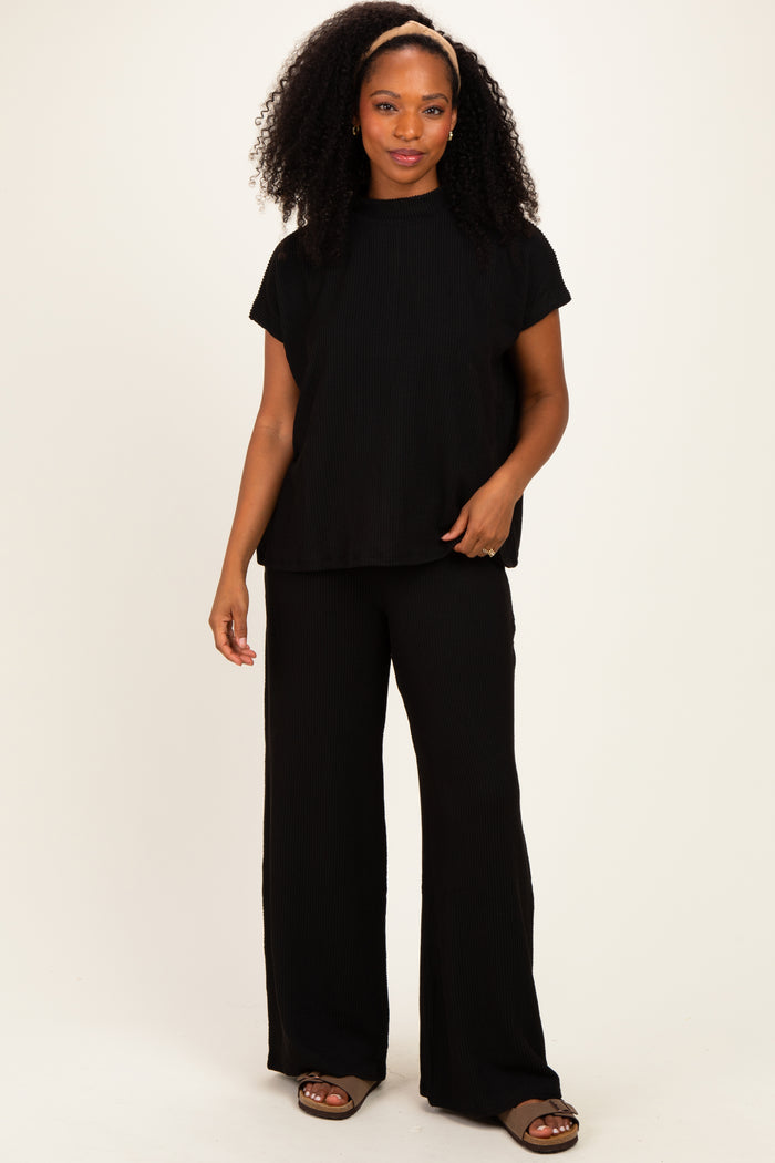 woman wearing a black ribbed short sleeve top and matching wide-leg pants, standing with one hand on her hip