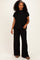 woman wearing a black ribbed short sleeve top and matching wide-leg pants, standing with one hand on her hip