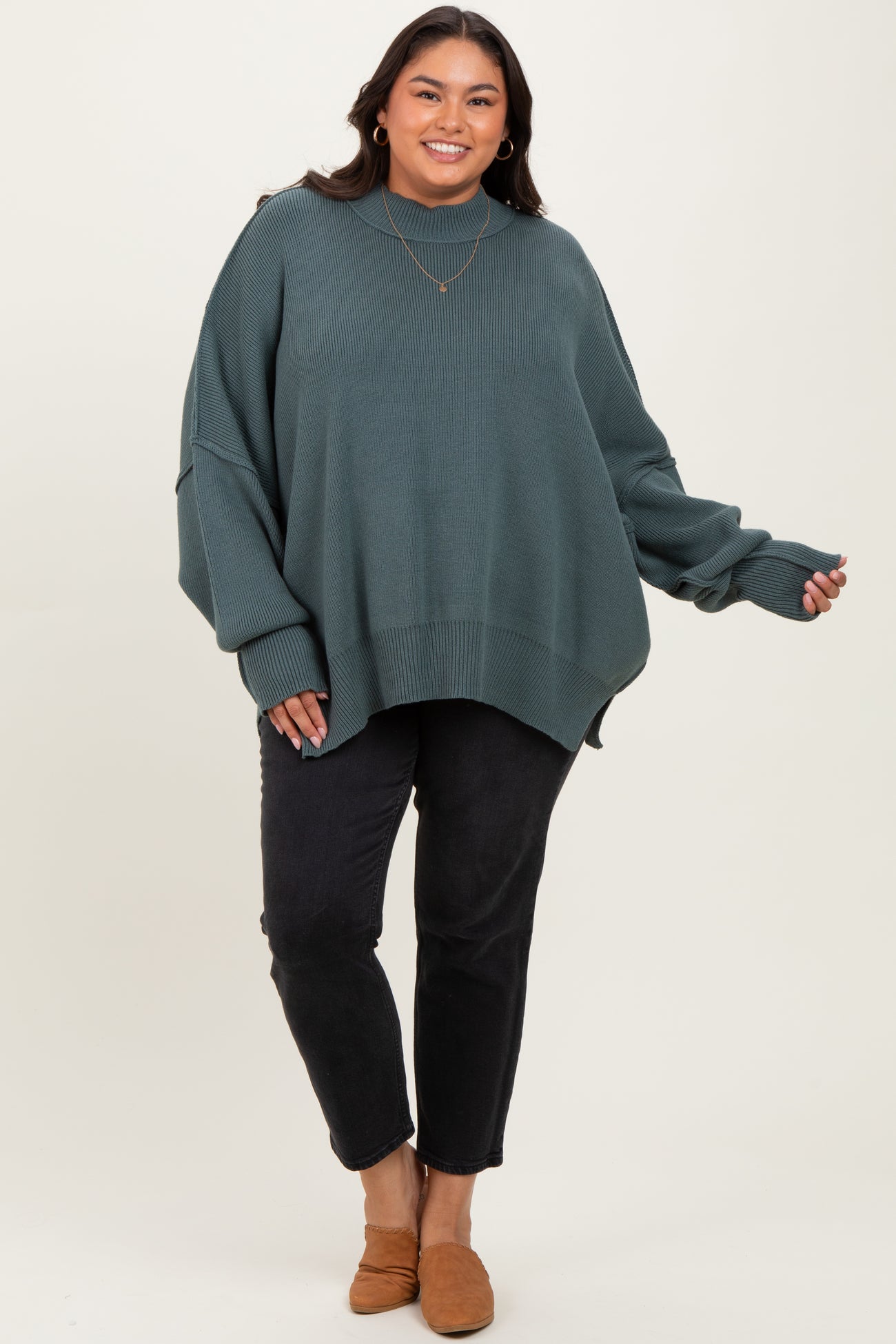 woman wearing a loose-fitting teal turtleneck sweater paired with black jeans and brown slip-on shoes