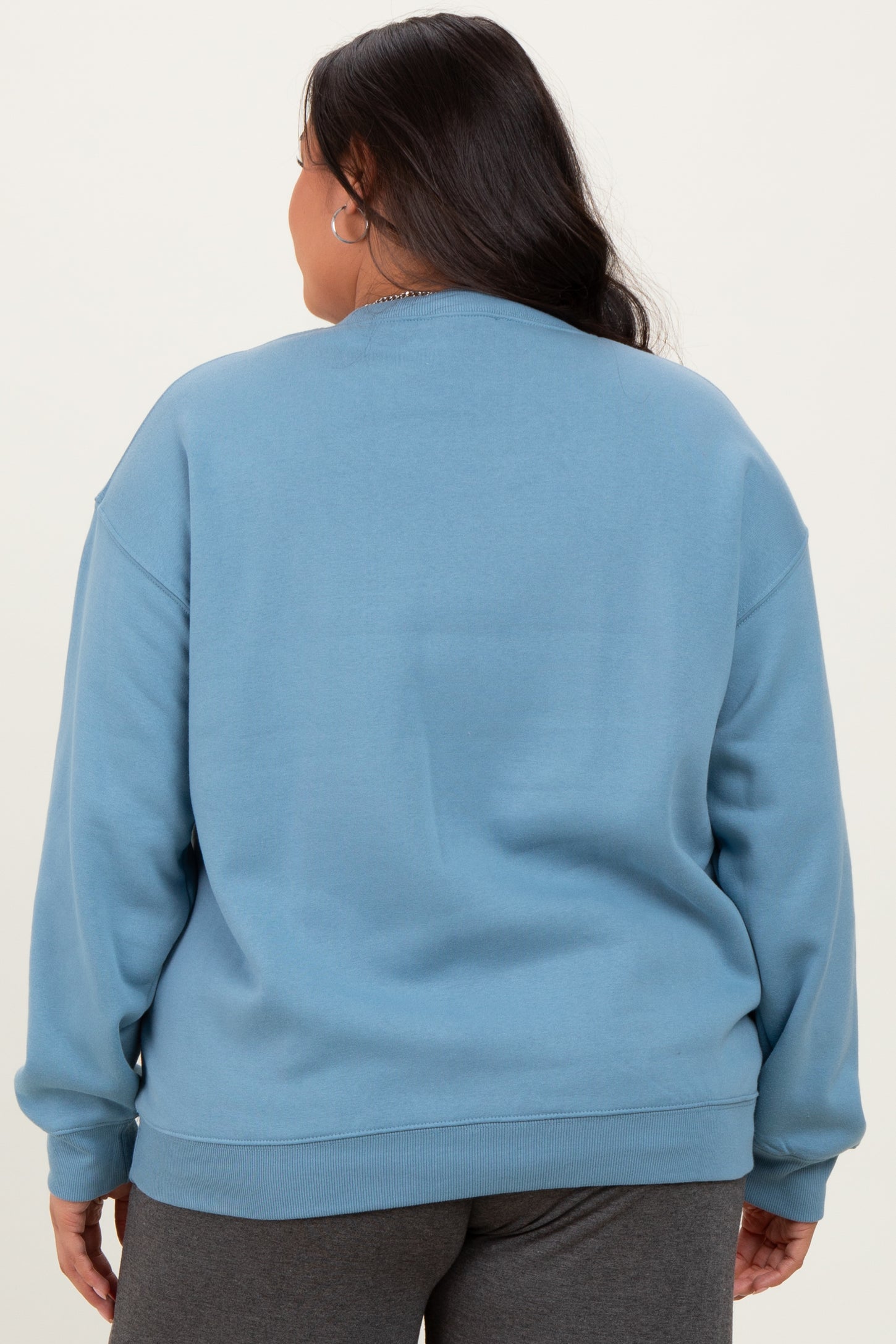 woman wearing a light blue oversized sweatshirt, view from the back, styled with gray sweatpants