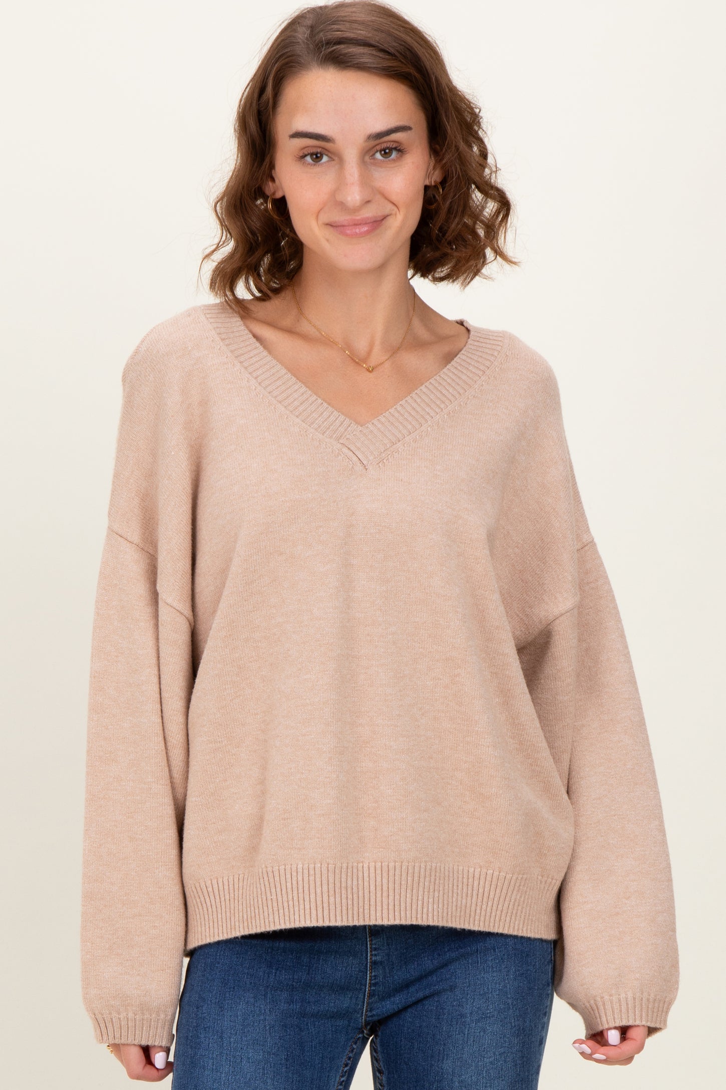 woman wearing a beige oversized v-neck sweater with long sleeves and relaxed fit, paired with blue jeans