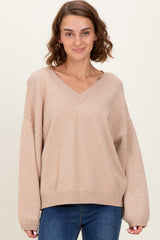 woman wearing a beige oversized v-neck sweater with long sleeves and relaxed fit, paired with blue jeans