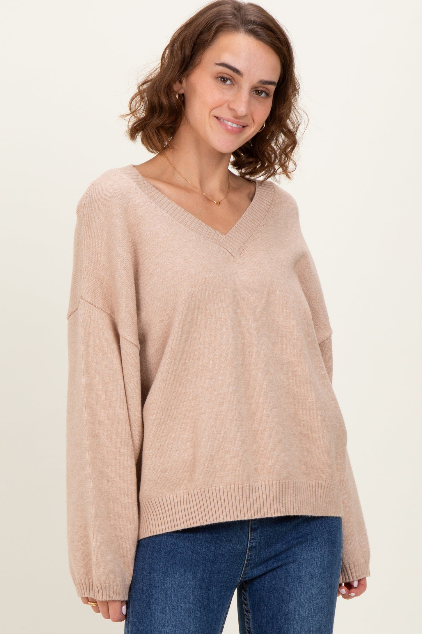 woman wearing a beige v-neck oversized sweater with long sleeves and a relaxed fit, paired with blue jeans