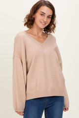woman wearing a beige v-neck oversized sweater with long sleeves and a relaxed fit, paired with blue jeans