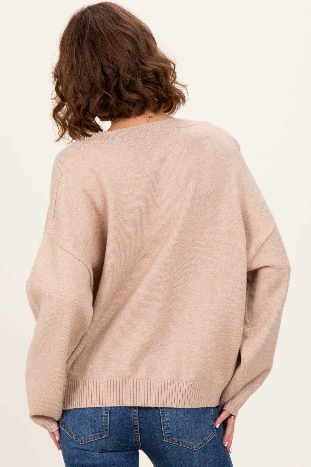 woman wearing a soft beige oversized sweater with a relaxed fit, styled with blue jeans, seen from the back