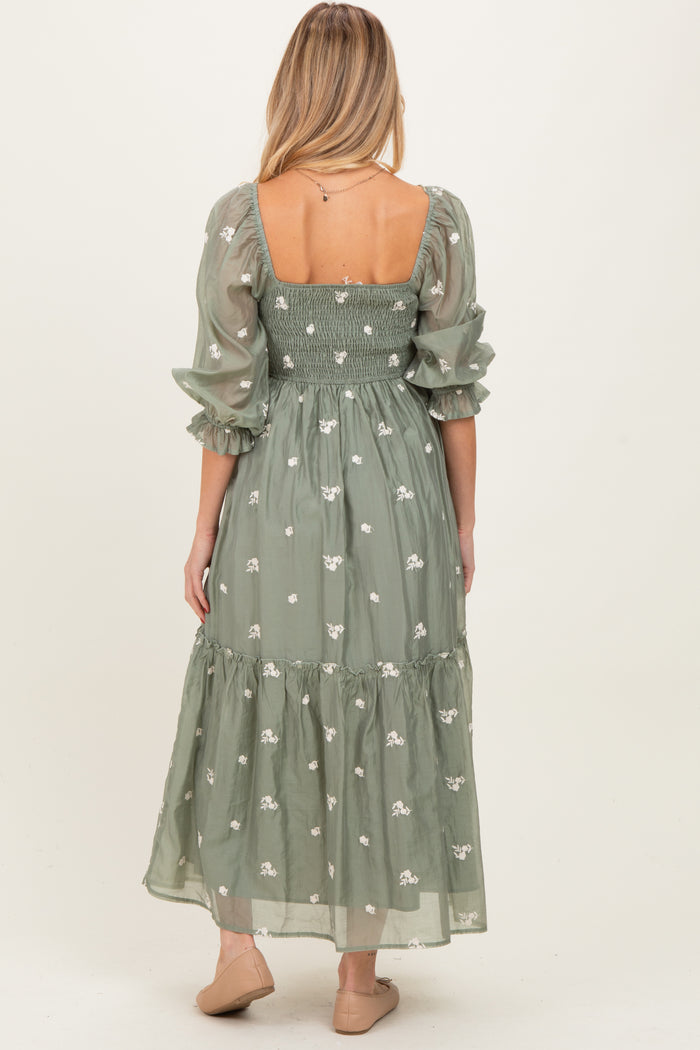 woman wearing a green embroidered maternity dress with puff sleeves and a long skirt, showcasing a baby bump from the back