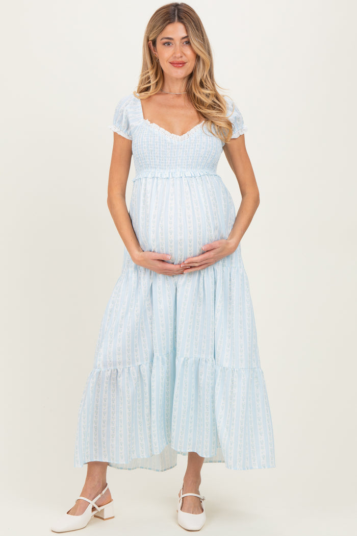 woman wearing a light blue maternity dress with short puff sleeves and a tiered skirt, holding her baby bump