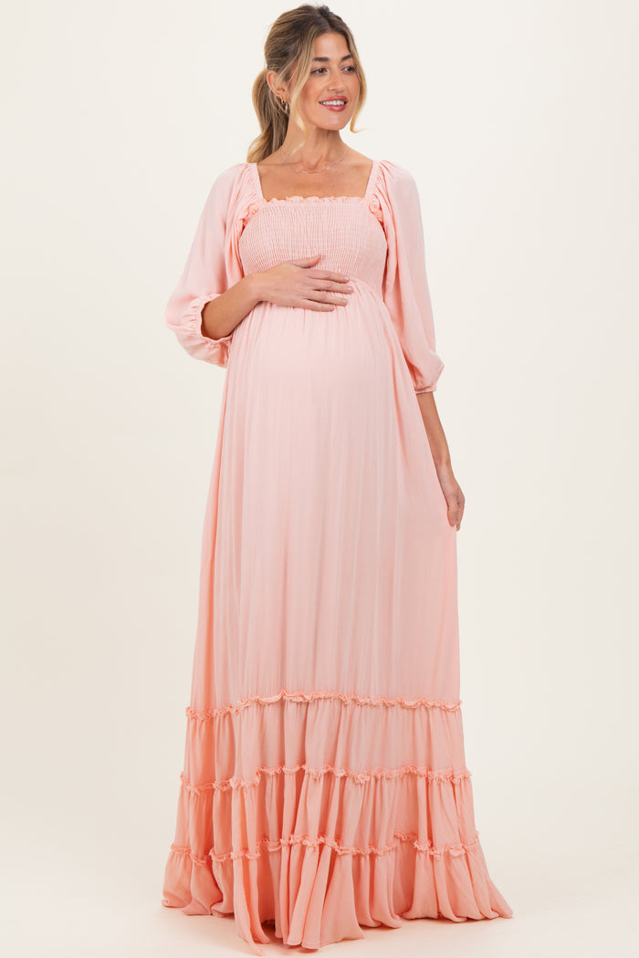 woman wearing a light peach maternity maxi dress with smocked bodice and tiered ruffle hem, holding her baby bump