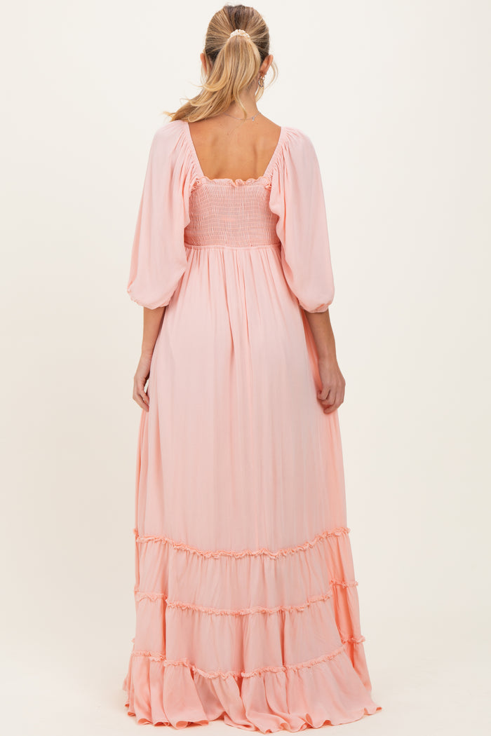 woman wearing a long pink maternity dress with smocked bodice and tiered ruffle hem, shown from the back