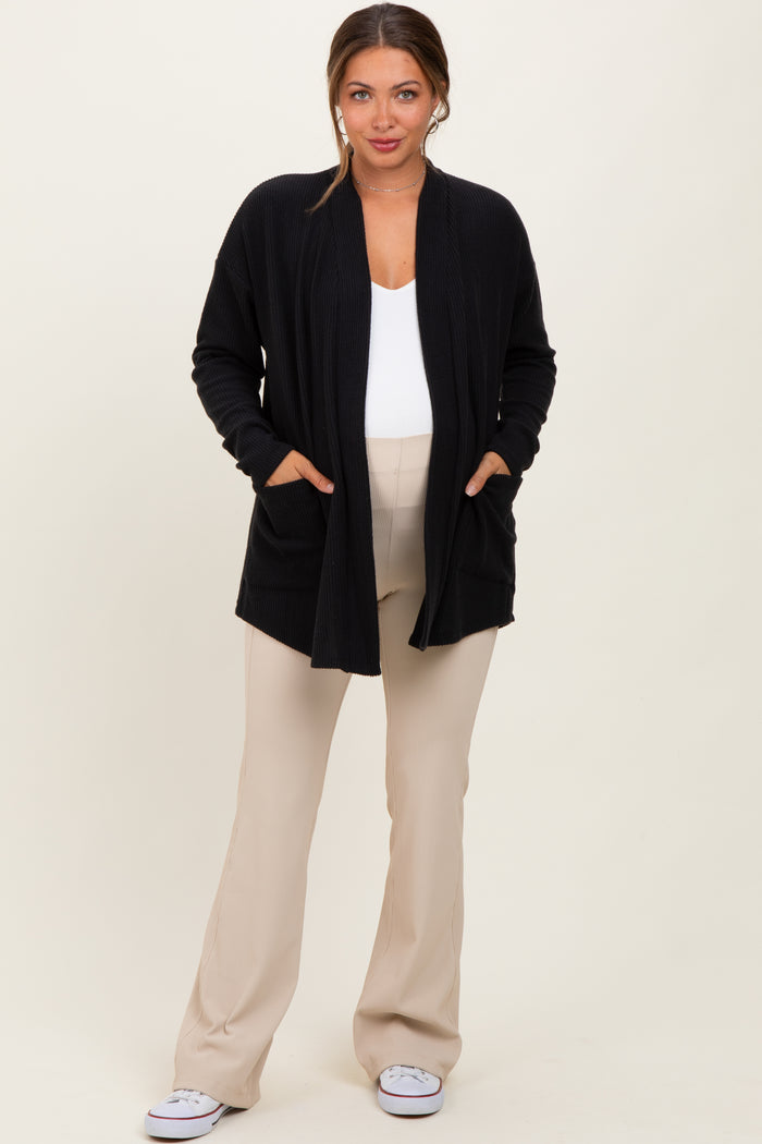 woman wearing a black open front maternity cardigan with pockets over a white top and beige maternity pants, showing her baby bump