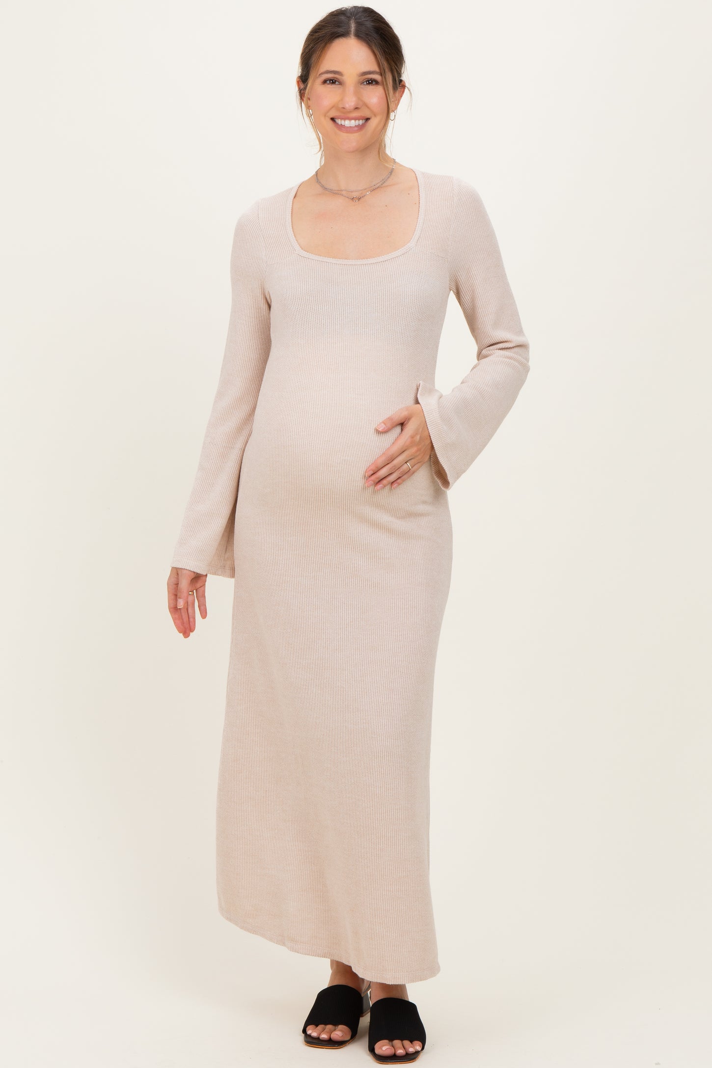 woman wearing a beige long sleeve maternity dress with a square neckline and holding her baby bump