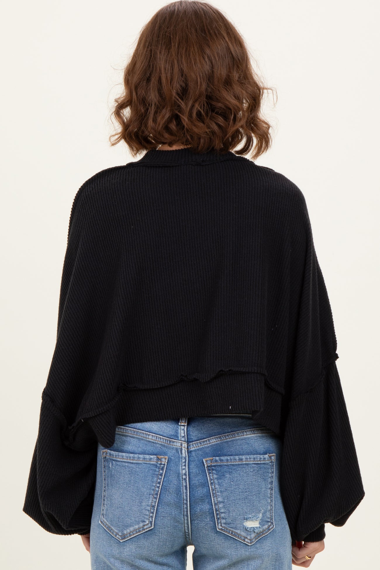 woman wearing a black oversized ribbed sweater with voluminous sleeves and a cropped back, styled with blue jeans