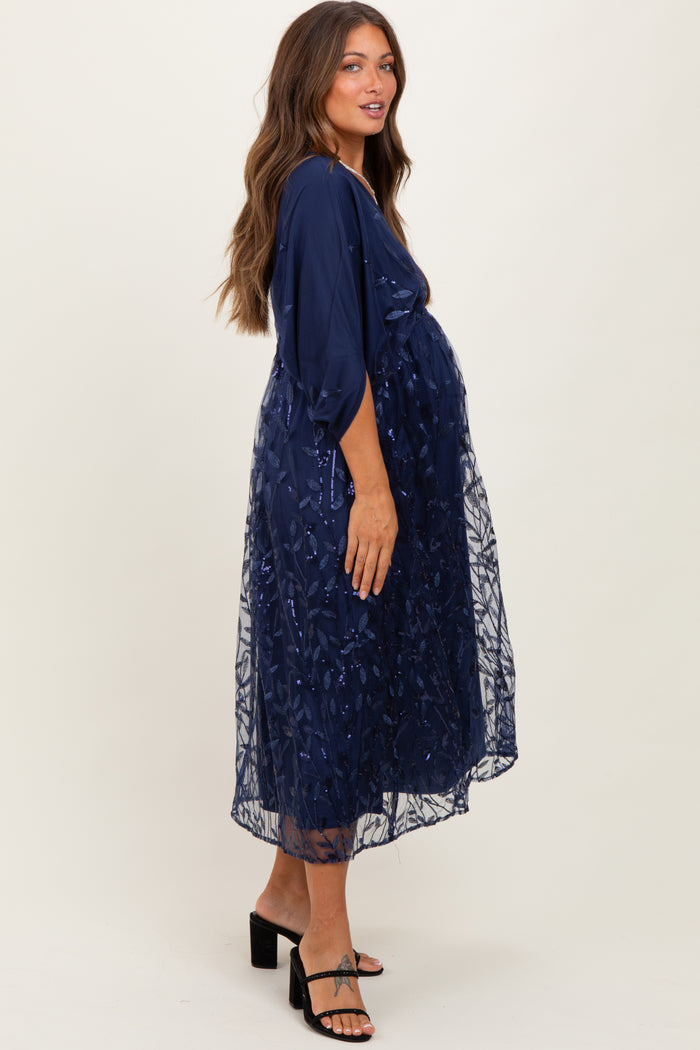 woman wearing a navy blue maternity dress with sheer overlay and embroidered details, showing her baby bump