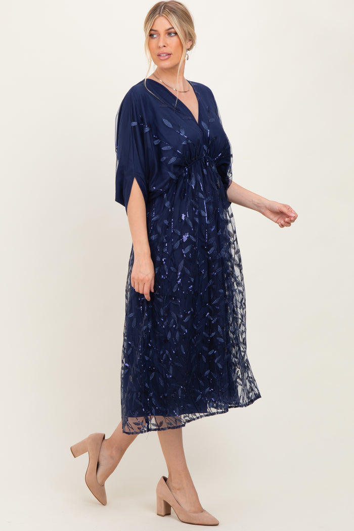 woman wearing a navy blue embroidered maxi dress with a cinched waist and flutter sleeves, paired with nude heels