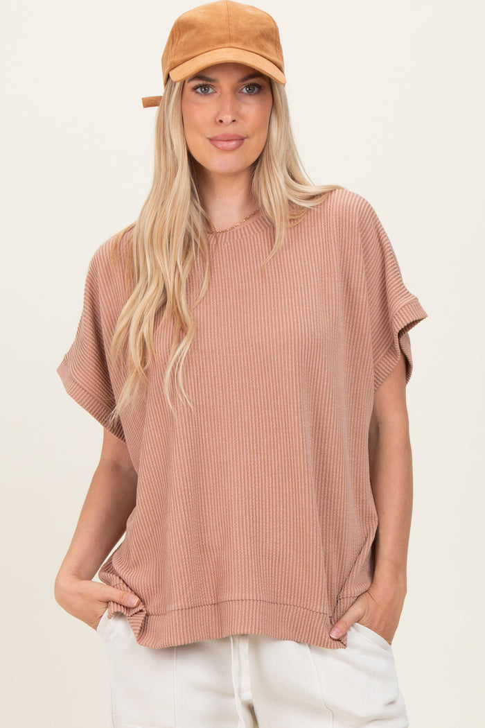 woman wearing a dusty rose oversized ribbed short sleeve top and a tan baseball cap, hands in pockets