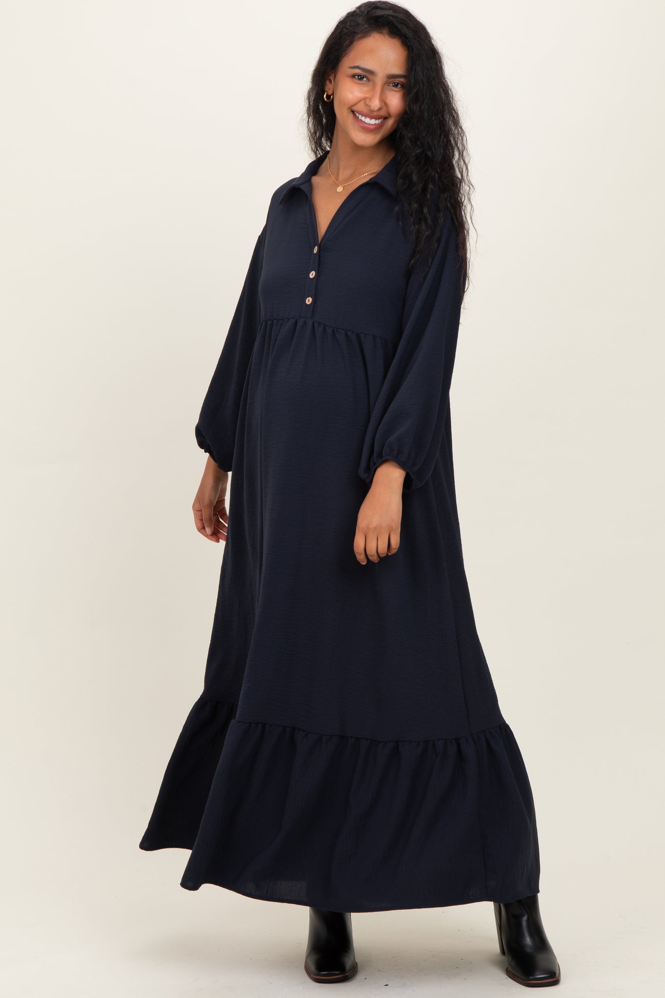 woman wearing a navy blue maternity maxi dress with a button-up collar and puff sleeves, showing her baby bump