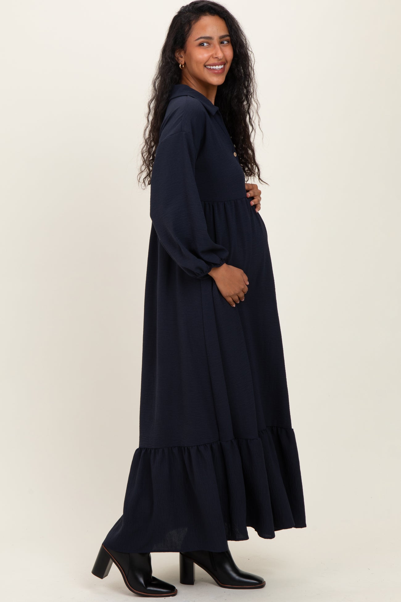 woman wearing a navy blue long sleeve maternity dress with a ruffled hem and cradling her baby bump