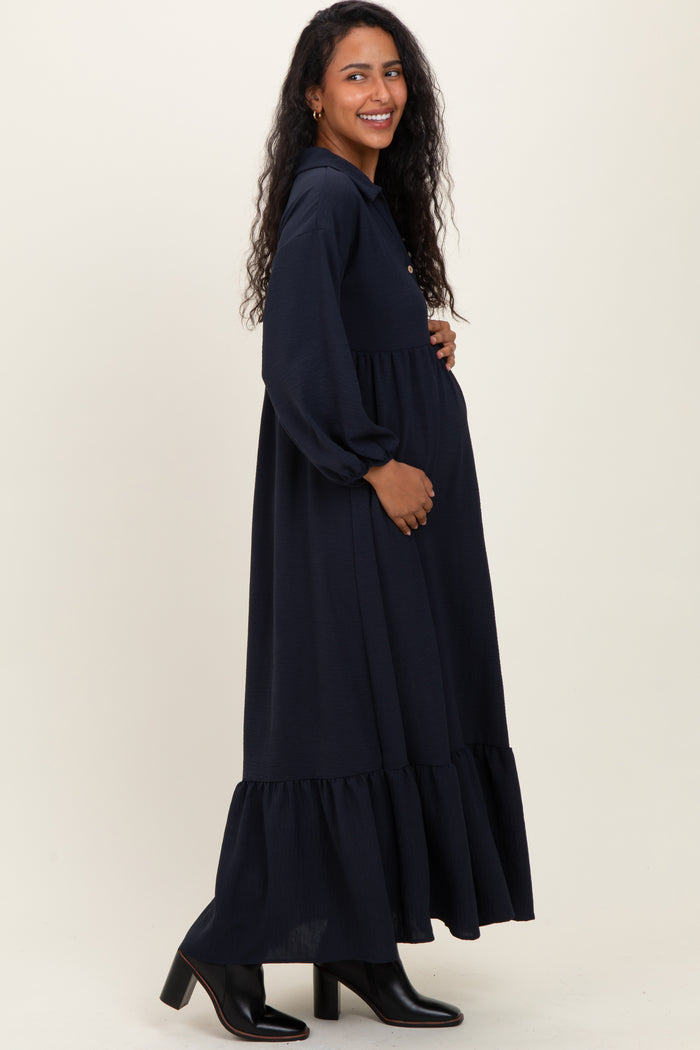 woman wearing a navy blue long sleeve maternity dress with a ruffled hem and cradling her baby bump