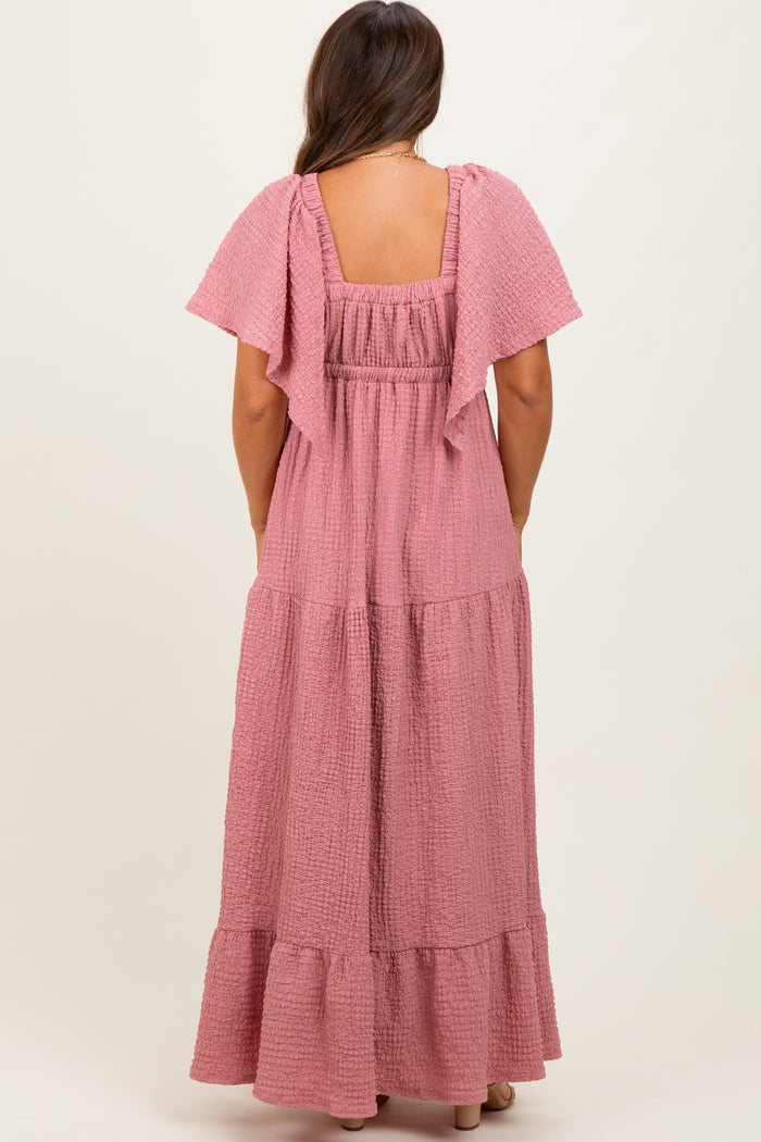 woman wearing a light pink maternity maxi dress with flutter sleeves and a tiered skirt from the back