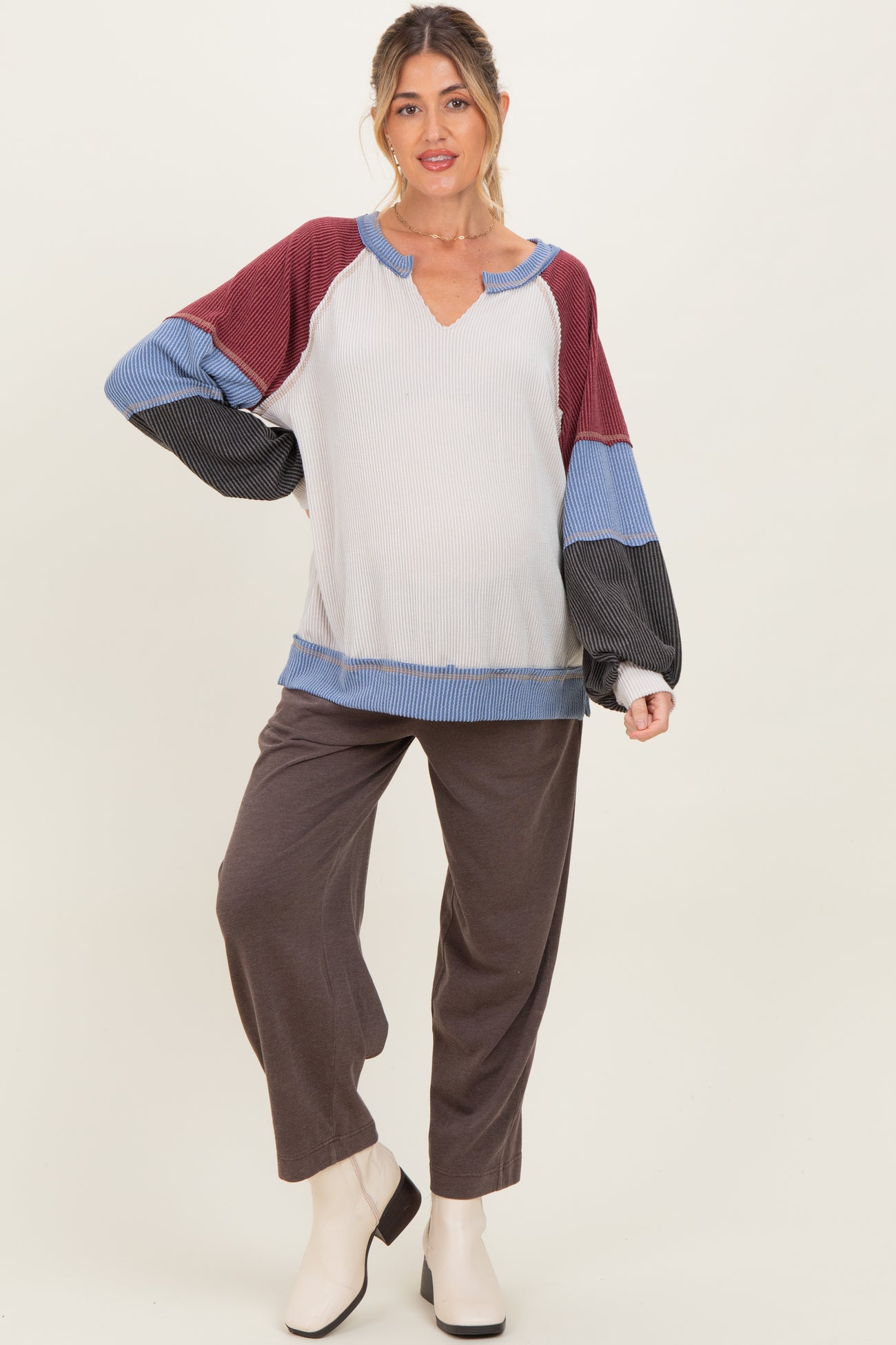 woman wearing a color-blocked maternity top with a v-neck and long sleeves, paired with gray wide-leg pants and a baby bump visible