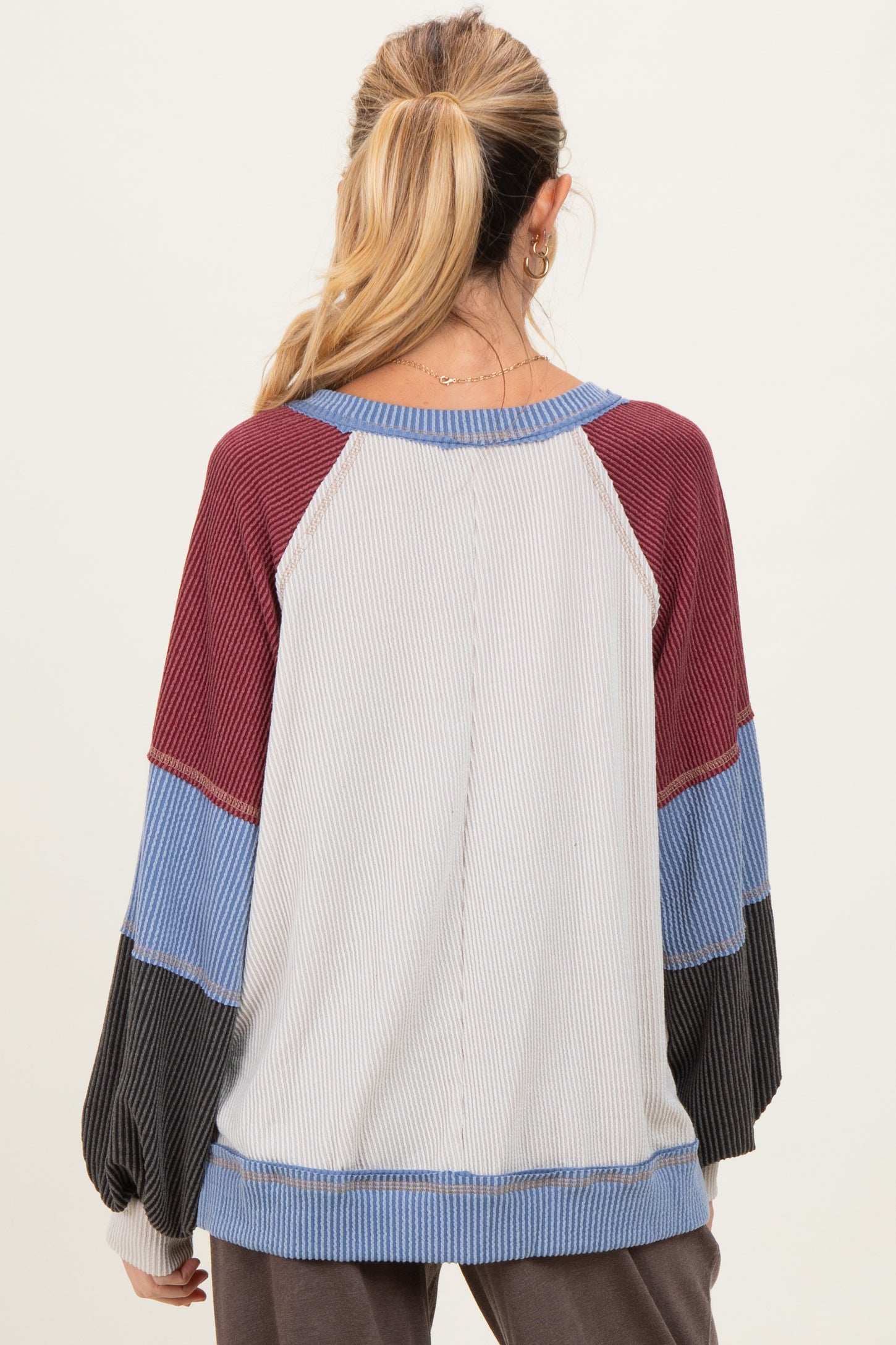 woman wearing a maternity color block long sleeve top in gray, maroon, blue, and black with a relaxed fit and balloon sleeves