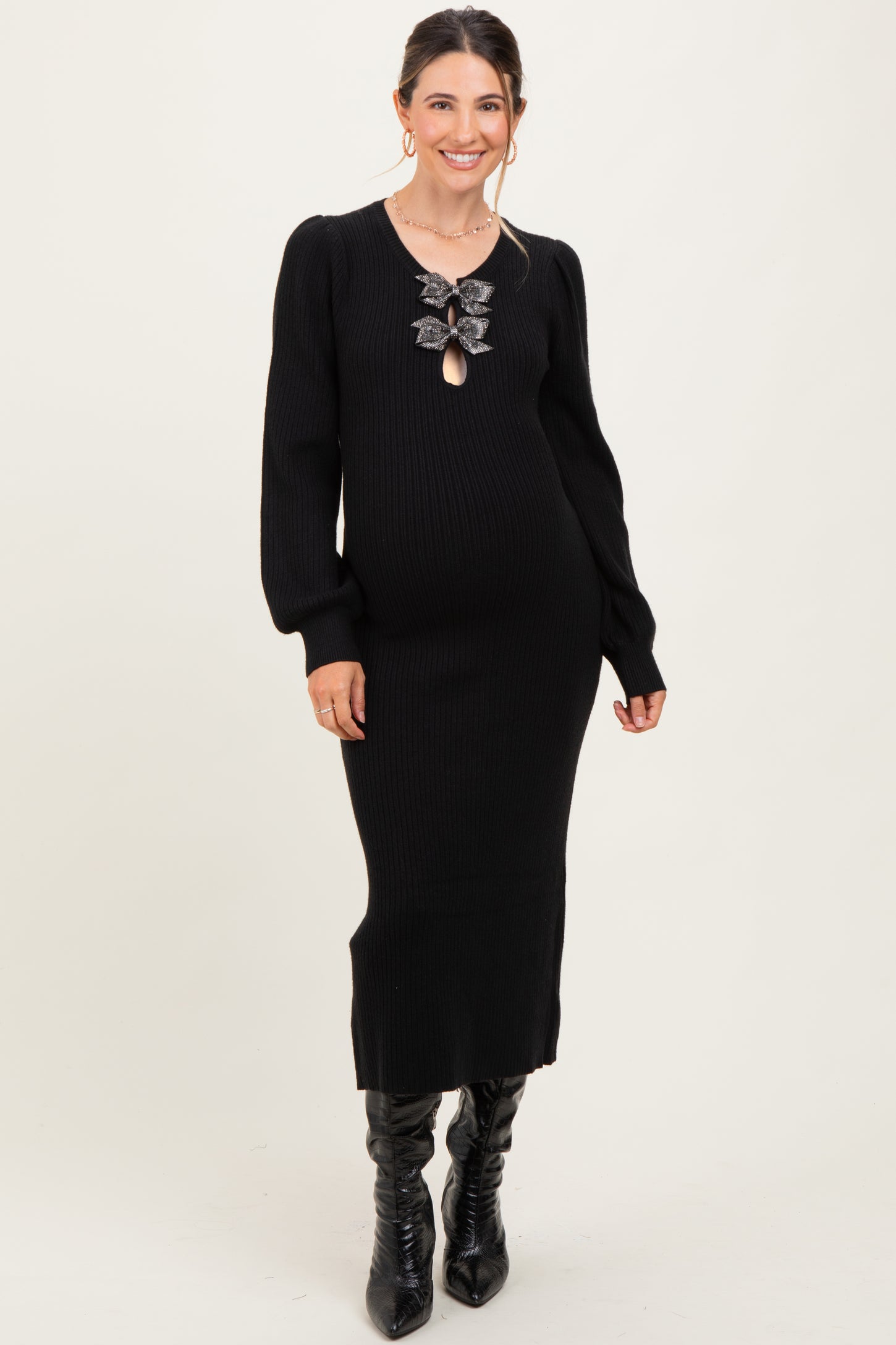 woman wearing a black long sleeve maternity dress with a keyhole detail and decorative bows, showcasing a baby bump