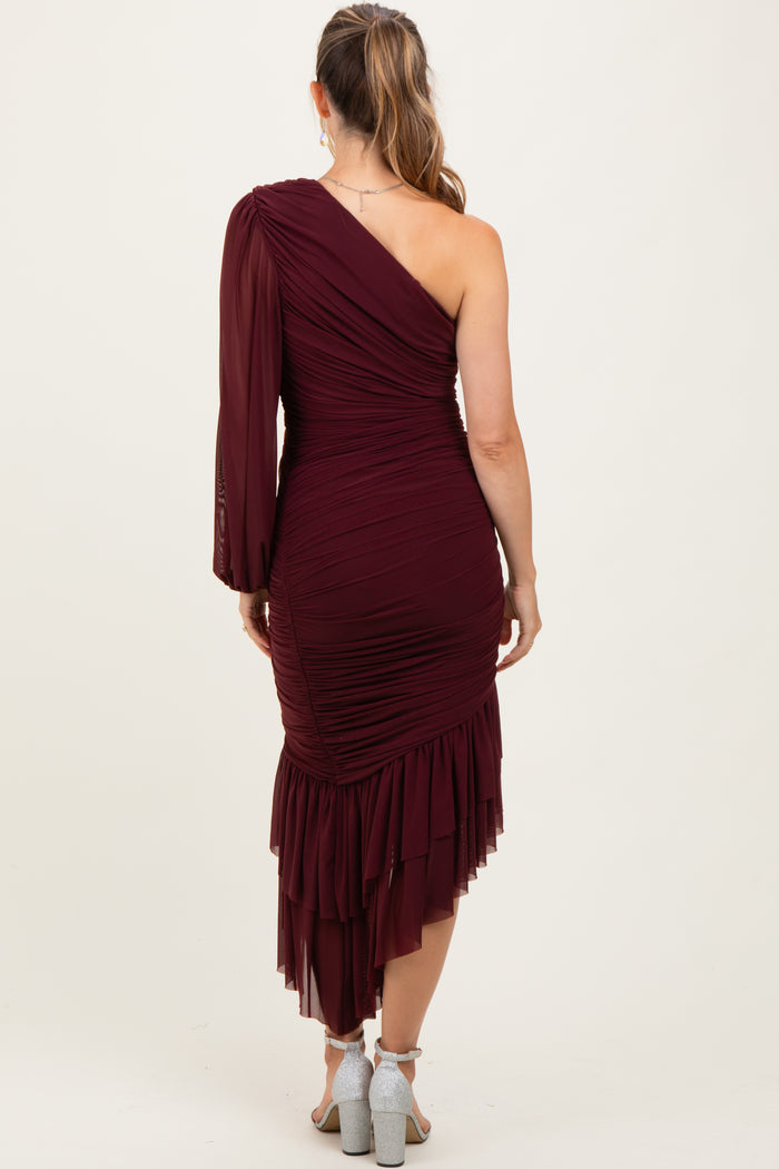 woman wearing a burgundy one-shoulder maternity dress with ruching and a ruffled hem, viewed from the back