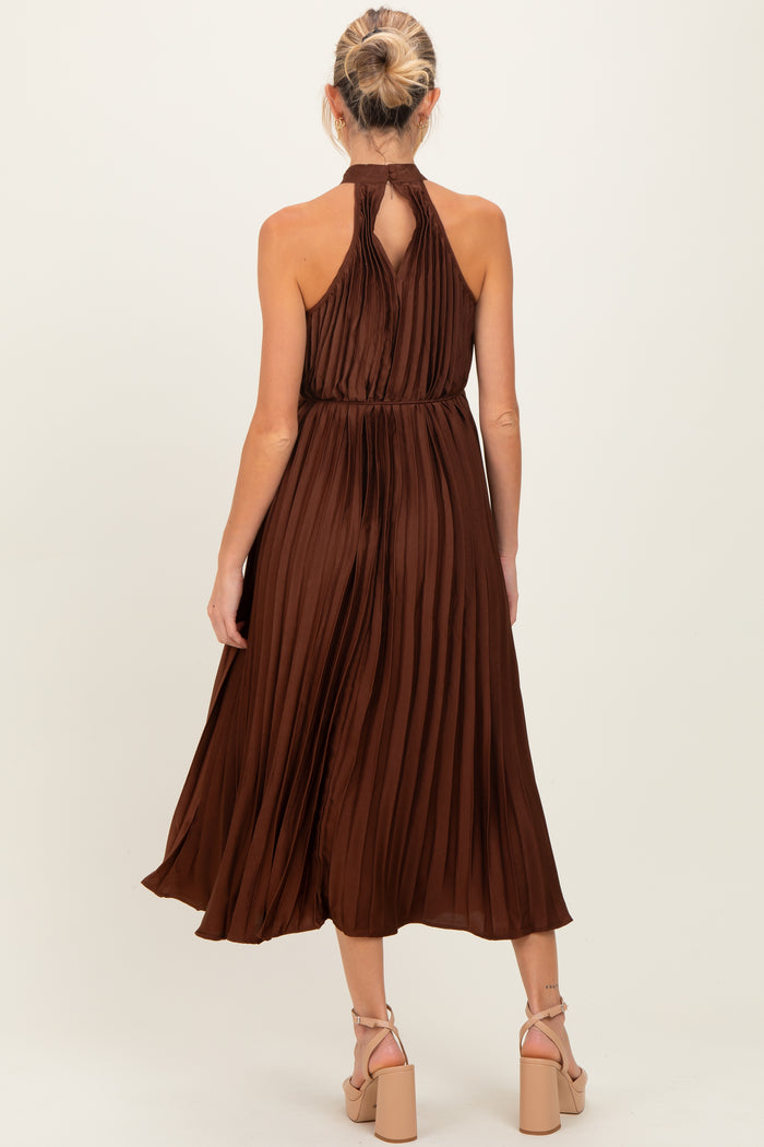 woman wearing a sleeveless brown pleated maternity dress with a halter neck and a flowy skirt, shown from the back