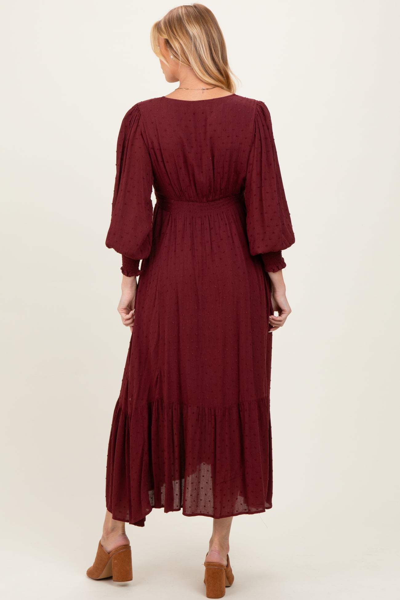 woman wearing a burgundy maternity dress with puff sleeves and a tiered hem, showing a baby bump from the back