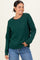 woman wearing a green cable knit sweater with a round neckline and relaxed fit, paired with denim jeans