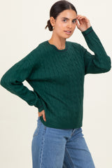 woman wearing a green cable knit sweater with a round neckline and relaxed fit, paired with blue jeans