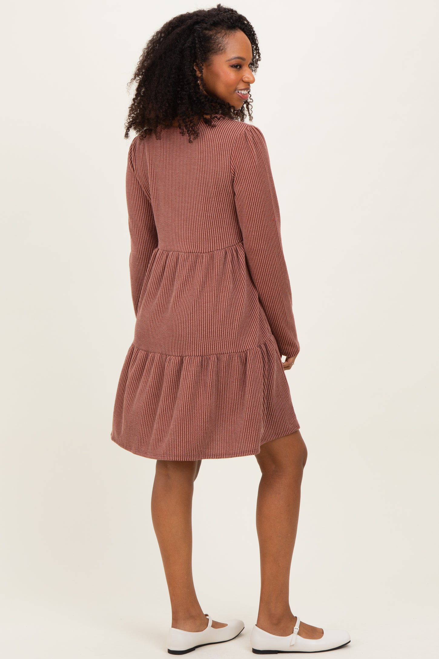 woman wearing a brown striped long sleeve dress with a tiered skirt and white flats, shown from the back