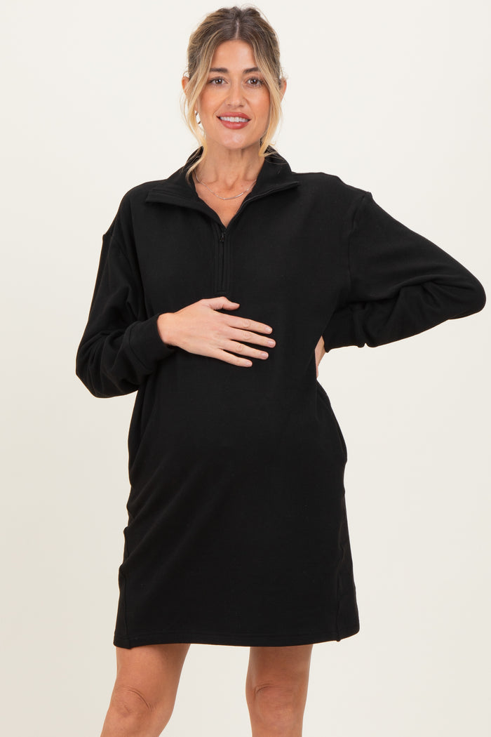 woman wearing a black maternity zip-up dress and holding her baby bump
