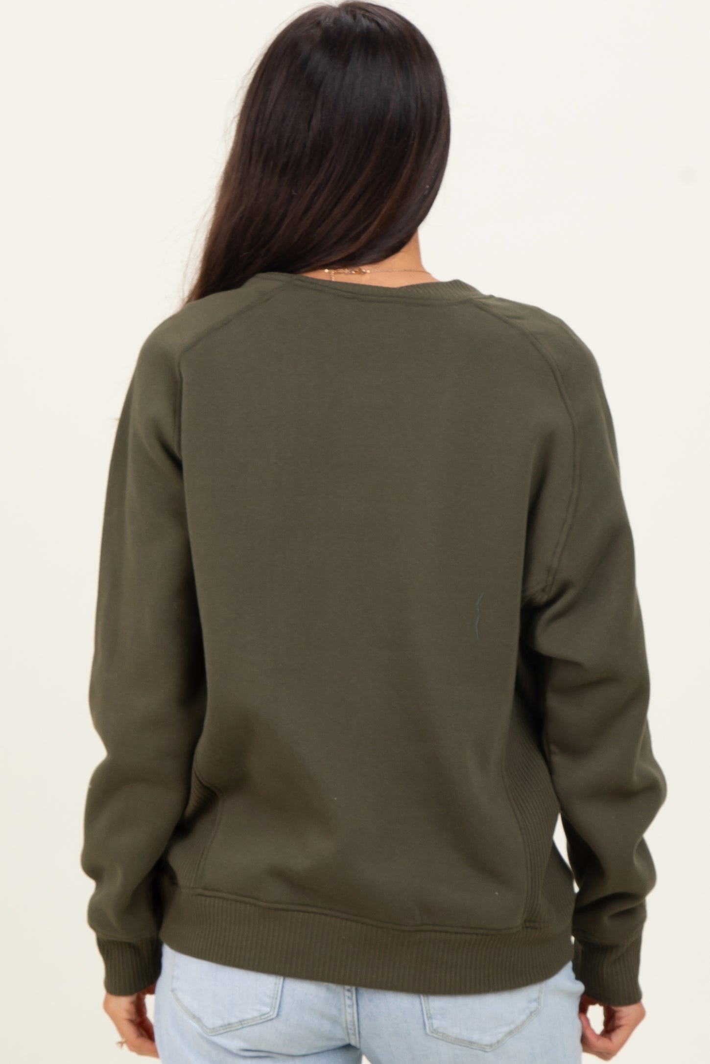 woman wearing a dark green long sleeve sweatshirt seen from the back with a relaxed fit and ribbed hem