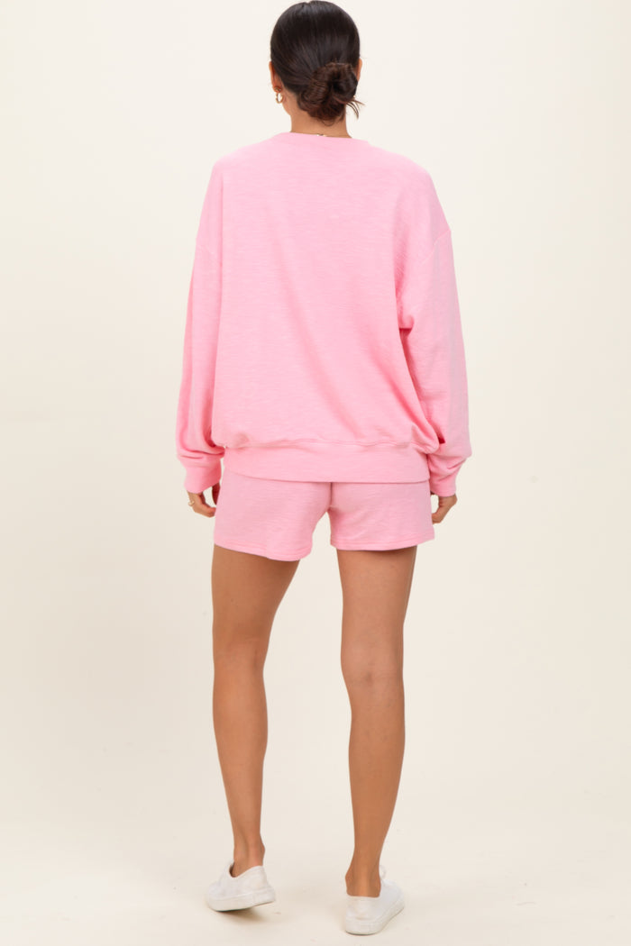 woman wearing a pink oversized sweatshirt and matching shorts, seen from the back