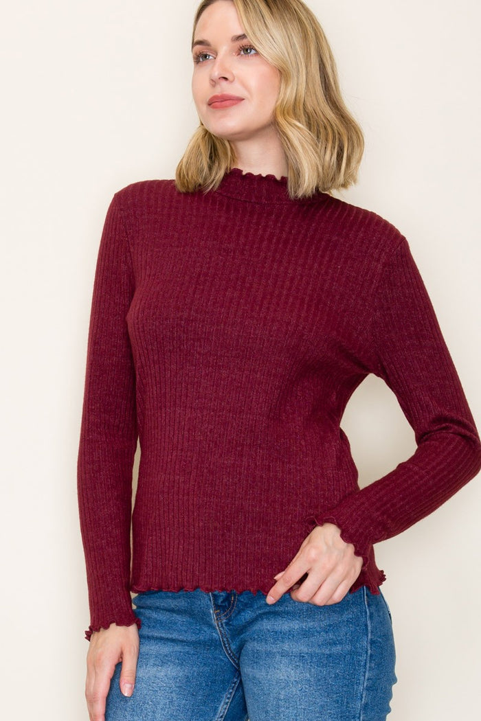 woman wearing a burgundy long sleeve ribbed top with a scalloped neckline and hem, paired with blue jeans