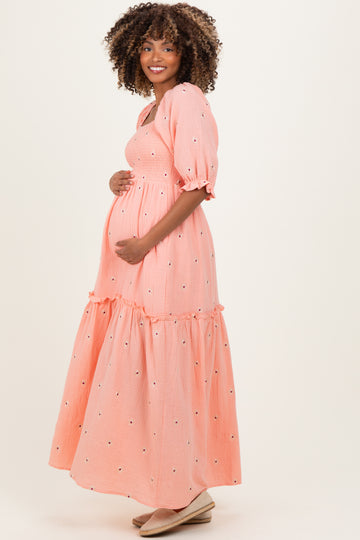 woman wearing a coral maternity maxi dress with a tiered skirt and puff sleeves, holding her baby bump