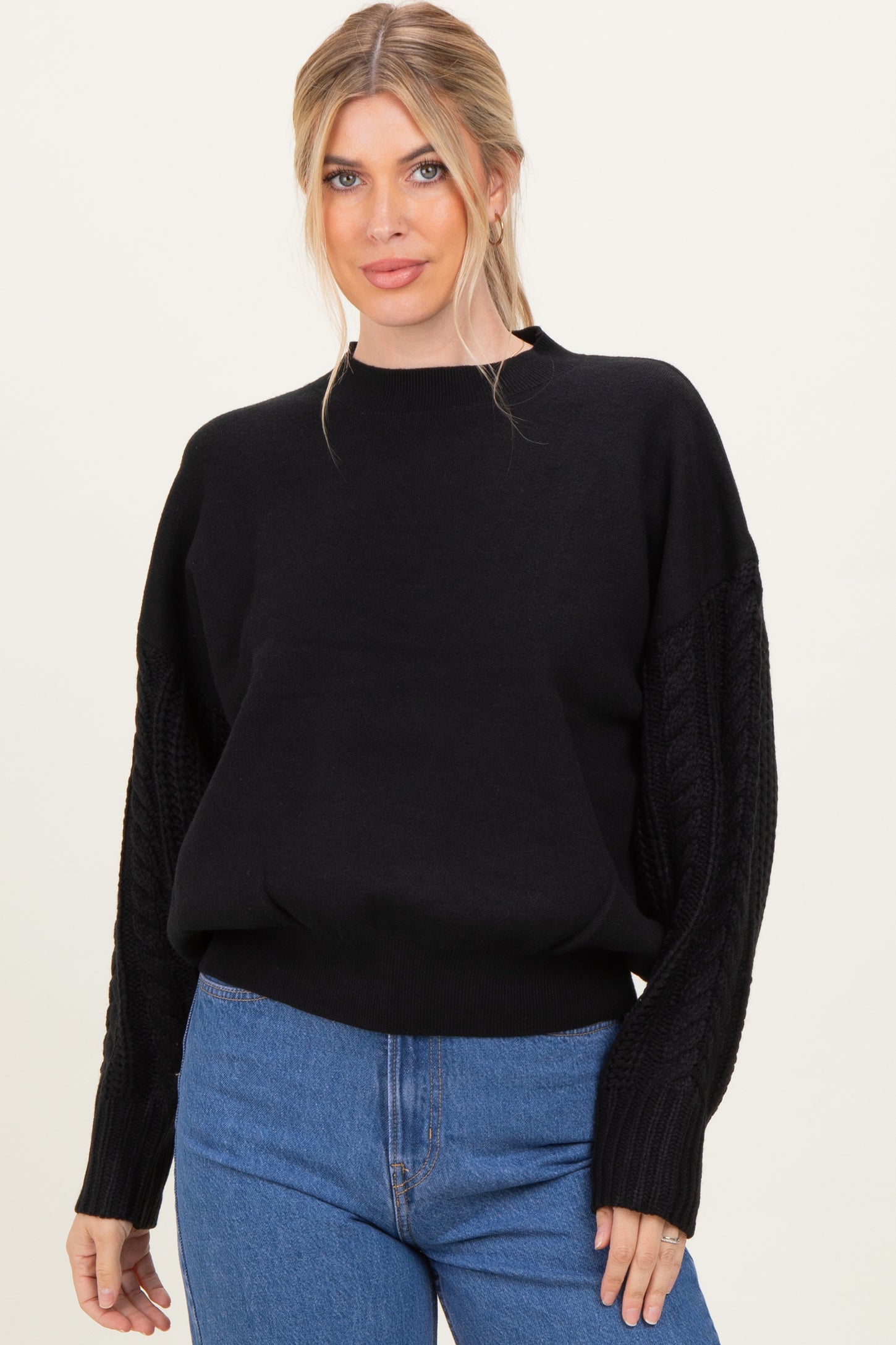 woman wearing a black oversized sweater with cable-knit sleeves paired with high-waisted blue jeans