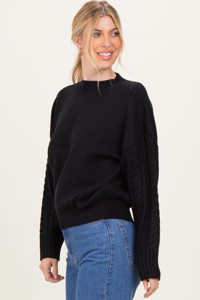 woman wearing a black sweater with cable-knit sleeves and a round neckline paired with high-waisted jeans
