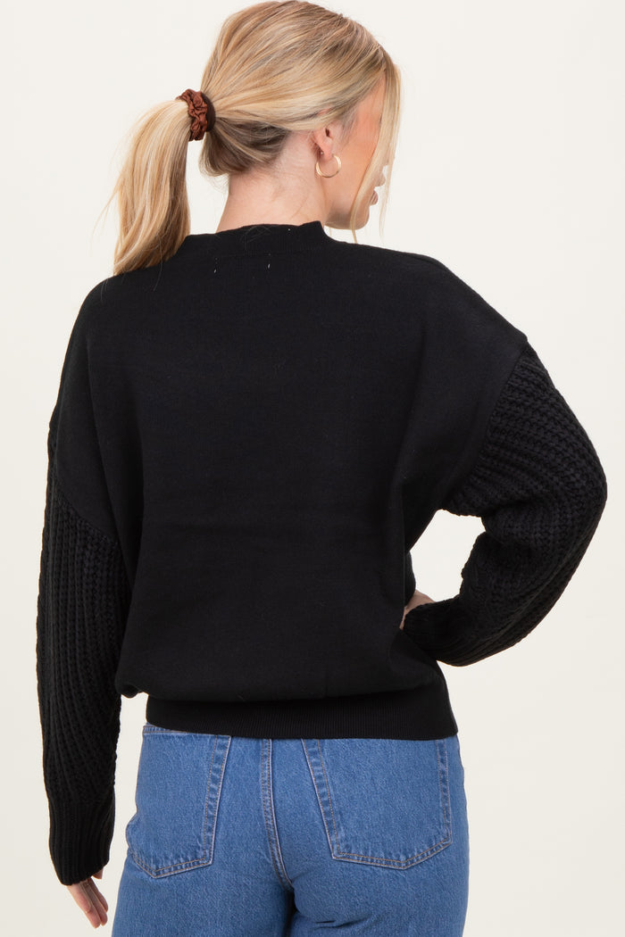 woman wearing a black oversized sweater with textured sleeves and a rounded neckline, seen from the back
