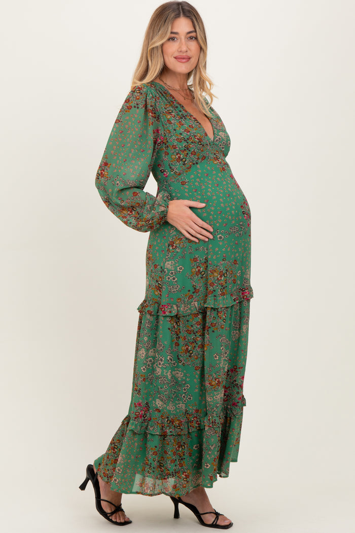 woman wearing a green floral maternity maxi dress with long sleeves and ruffles, cradling her baby bump